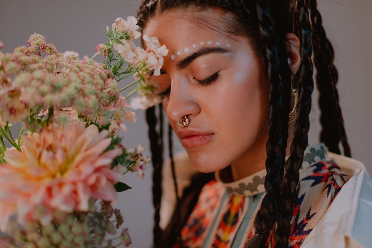 Home Artistic portrait of a woman with braided hair, surrounded by flowers, eyes closed, and a nose ring.