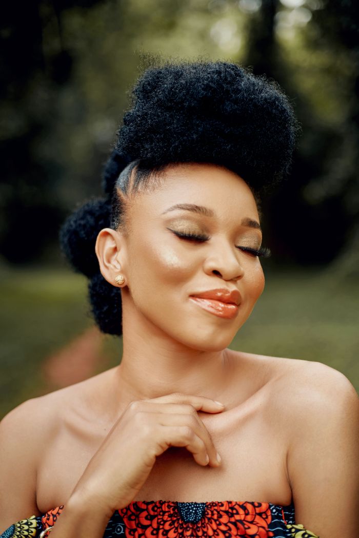 About Beautiful black woman with afro hair and closed eyes, smiling in a serene outdoor setting.