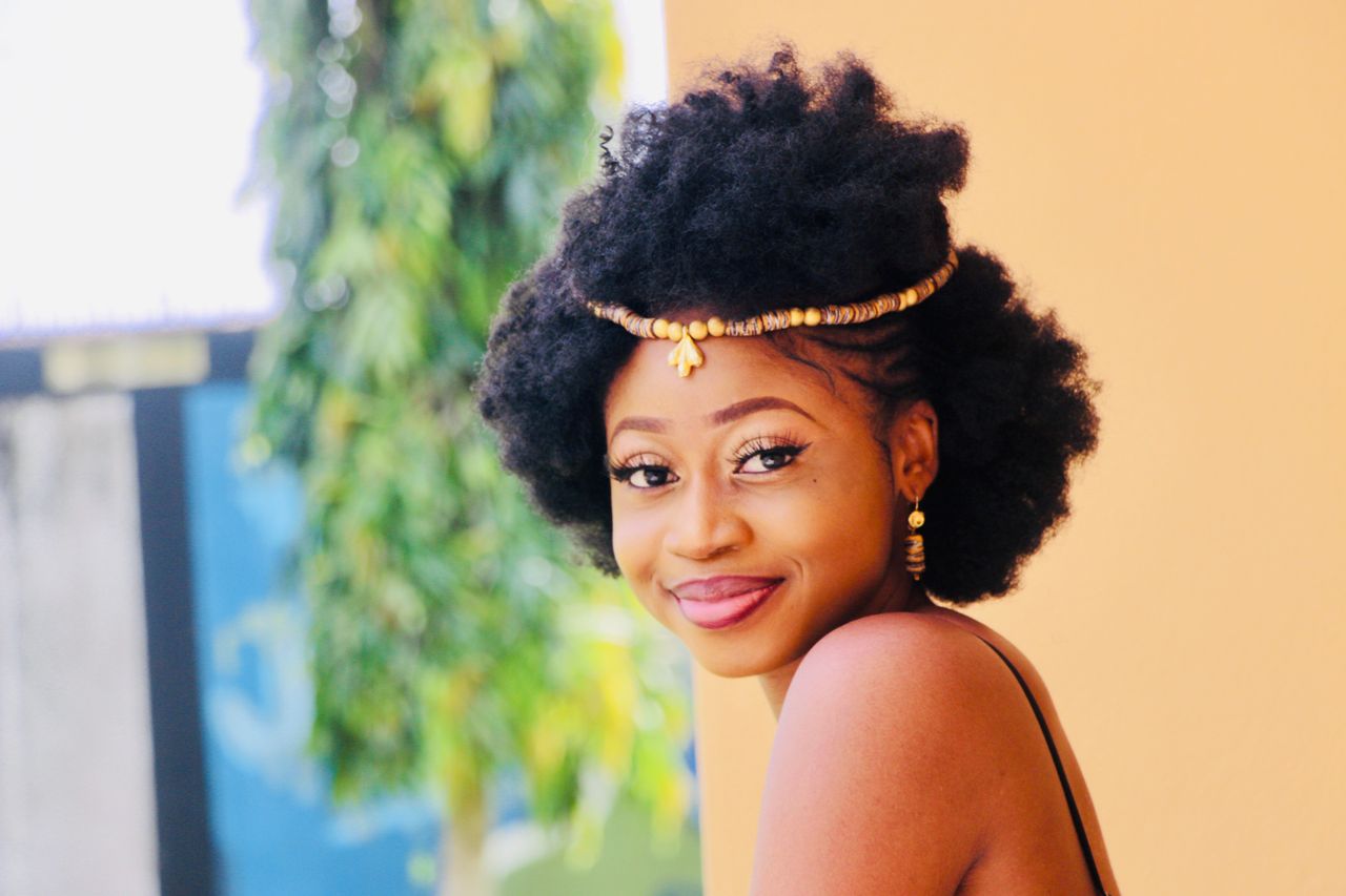 Home Optimistic young African American female with curly hair and gold accessories and makeup smiling and looking at camera