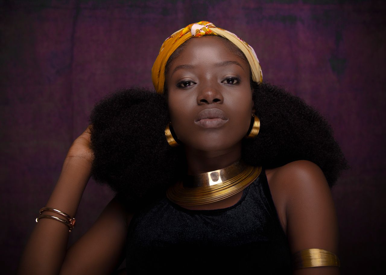 menu-01 Confident young ethnic female model wearing traditional accessories and headband touching Afro hair and looking at camera against purple background