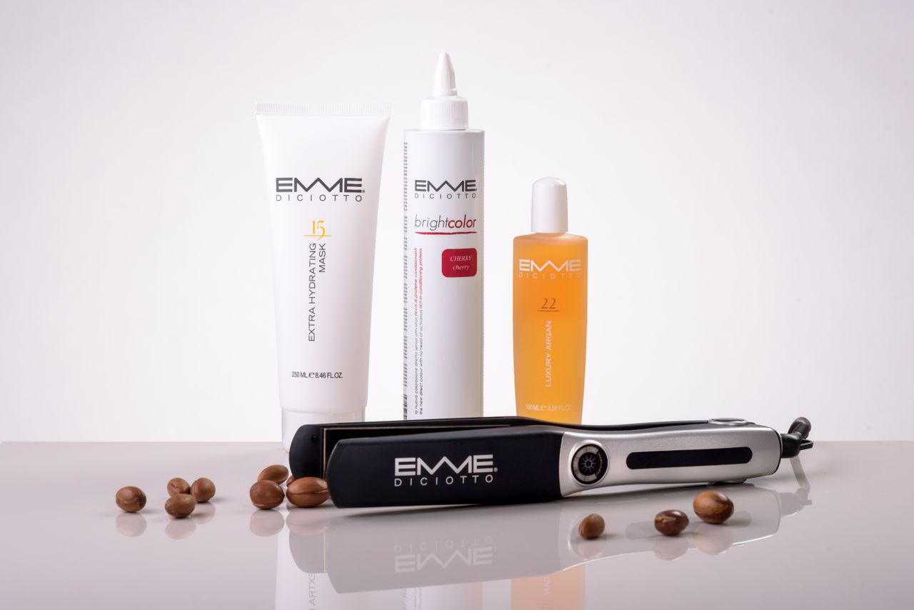 Home Hair care products and a flat iron by EMME Diciotto on a reflective surface for beauty routines.